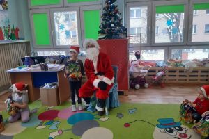 Mikołaj przy choince i przedszkolak trzymający prezent
