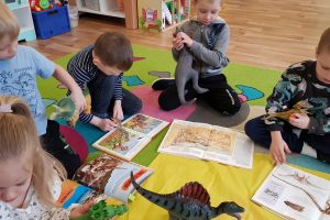 Dzieci siedzą na dywanie i oglądają książki o dinozaurach