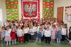 duża grupa przedszkolaków stoi pod godłem Polski